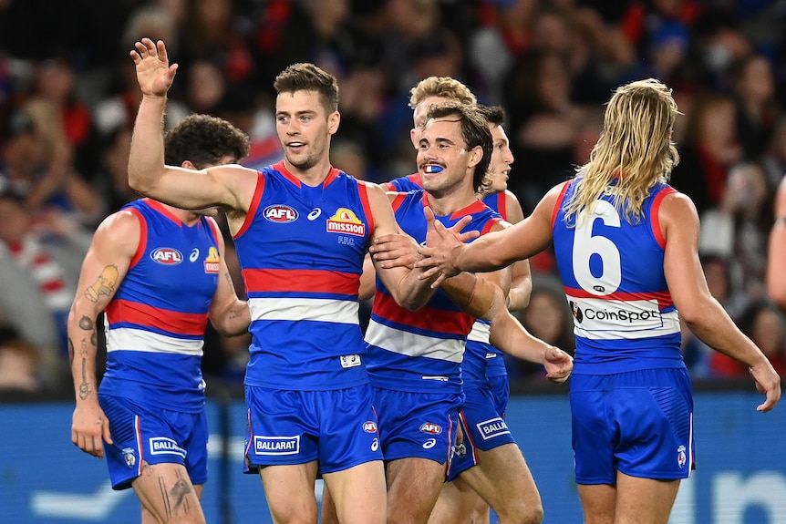 Josh Dunkley holds his hand up for a high five as other teammates in blue singlets grab him from behind