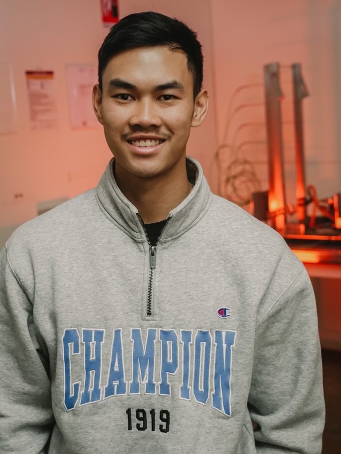 Man with dark hair wearing a grey jumper with the word "champion" printed on it. 