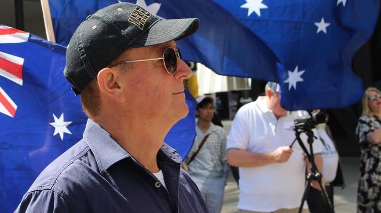 Fraser Anning stands in front of Australian flags.