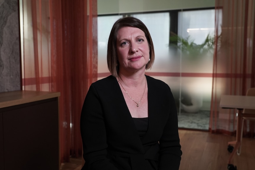 Cynthia Gebert is wearing black and smiling for a portrait in a dark office.