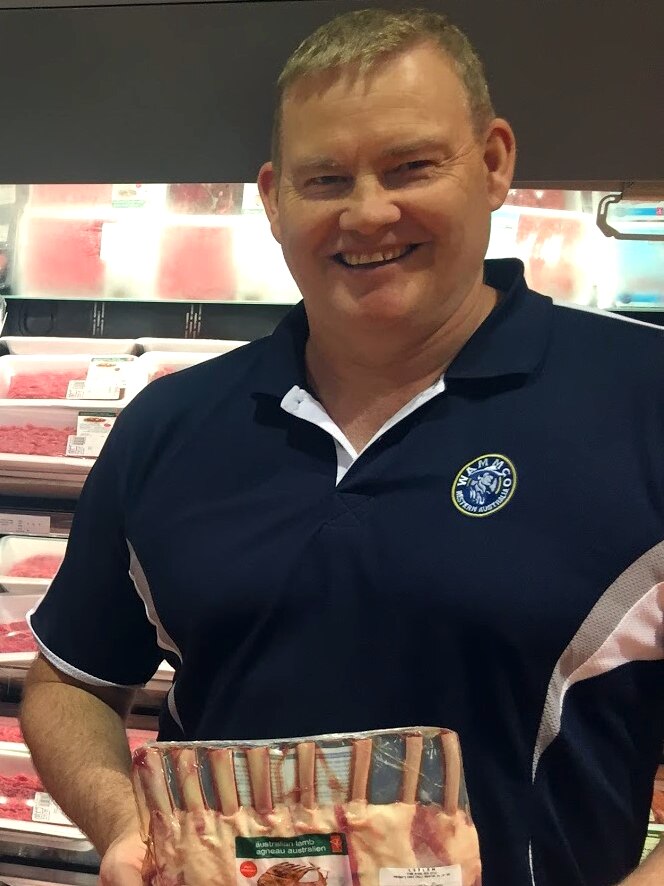 A man stands in front of the meat section at a supermarket holding a rack of lamb cutlets
