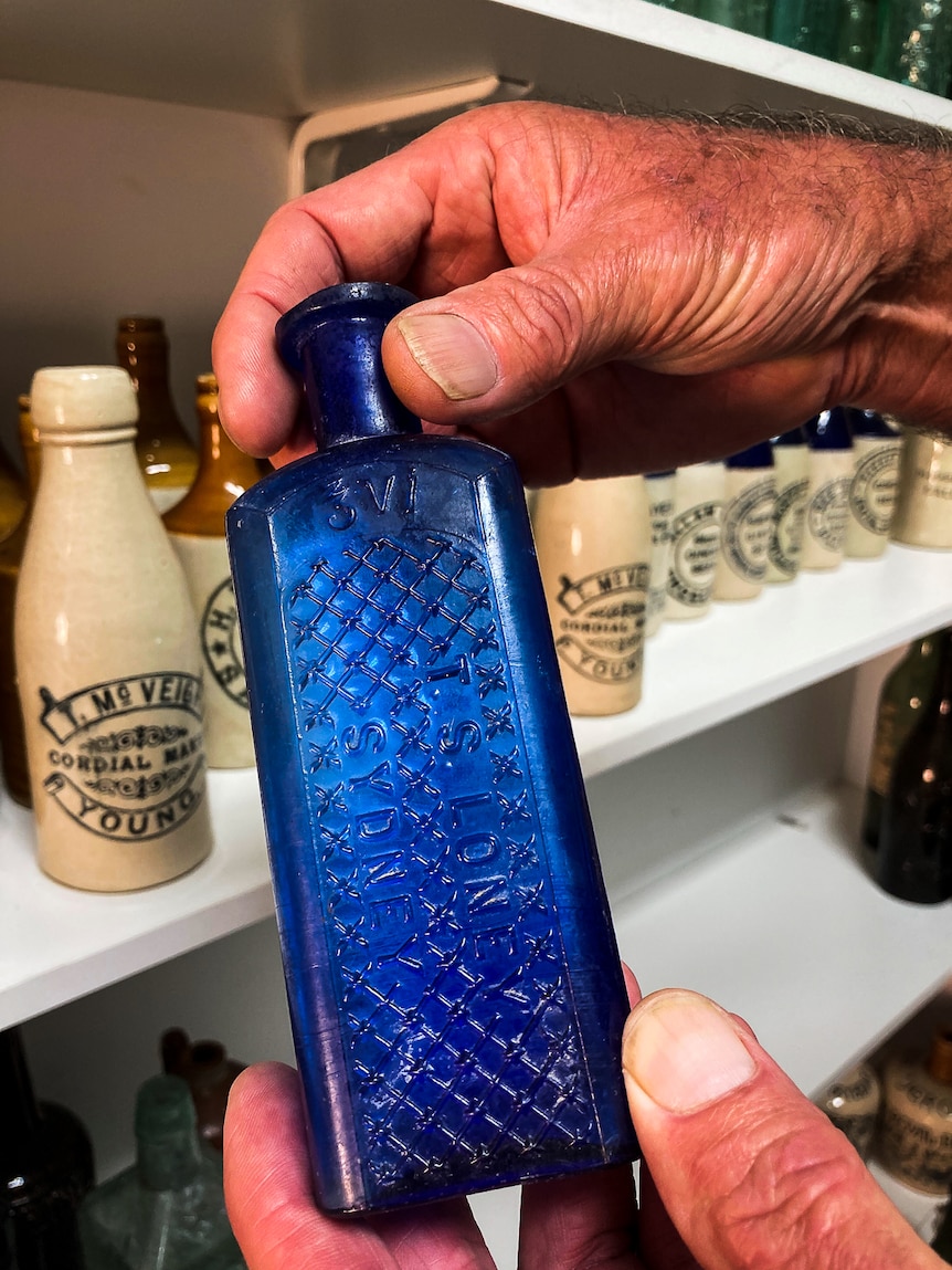 Hands holding blue bottle that once held poison, inscribed T.S Loney Sydeny