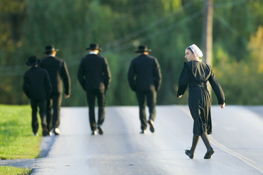 A young Amish girl walking behind a group of Amish men