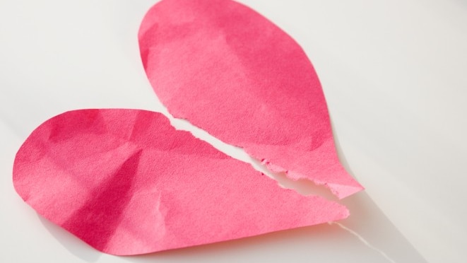 Crumpled pink paper heart cutout torn in two