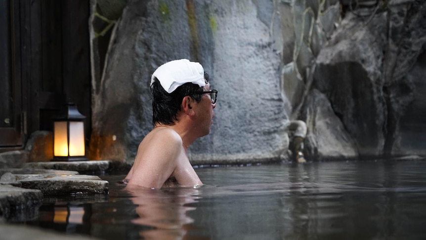 A man with a towel on his head floats blissfully in a Japanese hot spring