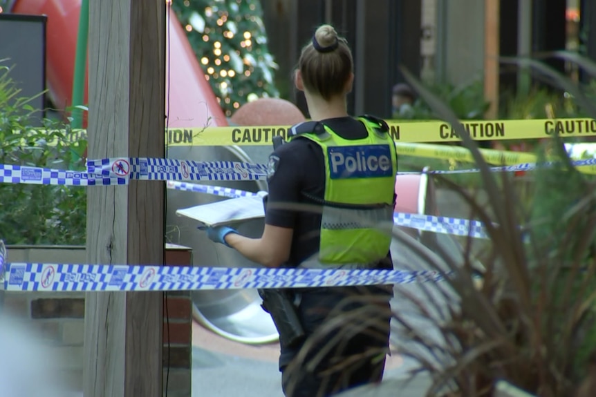 A police officer stands near police tape.