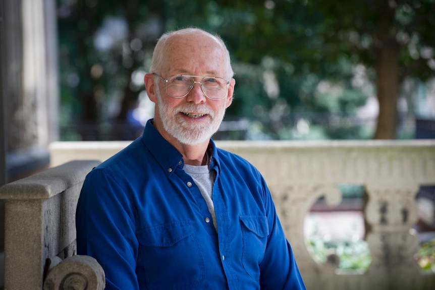 Portrait of a man with a grey beard smiling with glasses on.