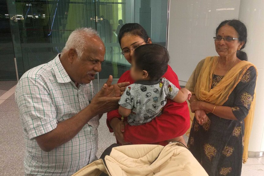 Srihari's Dad leaning in to talk to his grandson, while Srihari's mother and wife look on.