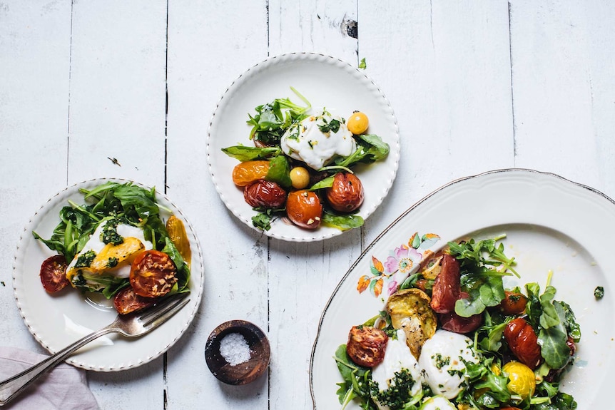 Roast caprese salad recipe with rocket leaves, mozzarella, tomatoes and basil oil served on small plates as a summer side.