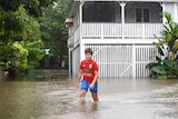 A boy wading through floodwater outside an old Queenslander house