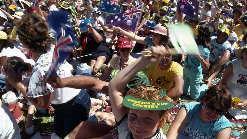 A boy waves a flag over his head in amongst a huge crowd, some with Australian flags