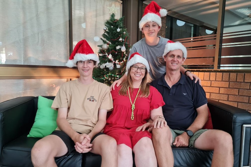 Two boys and their parents with santa hats on smiling in front of a christmas tree. 