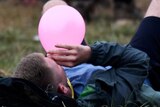 A festival-goer lying on the ground on his back inhaling nitrous oxide through a balloon