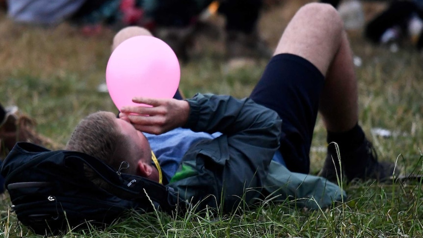 A festival-goer lying on the ground on his back inhaling nitrous oxide through a balloon