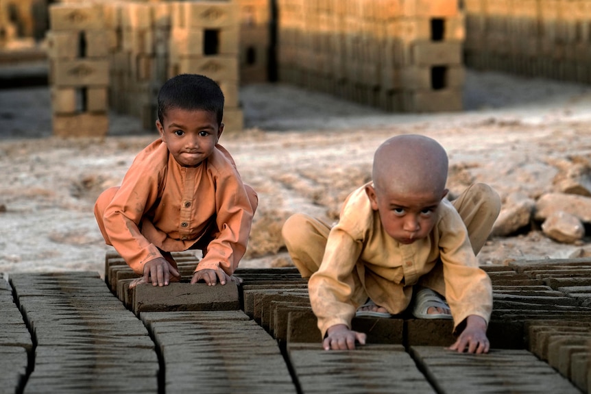 two afghan children sit on a pile of bricks while working in a brick factory
