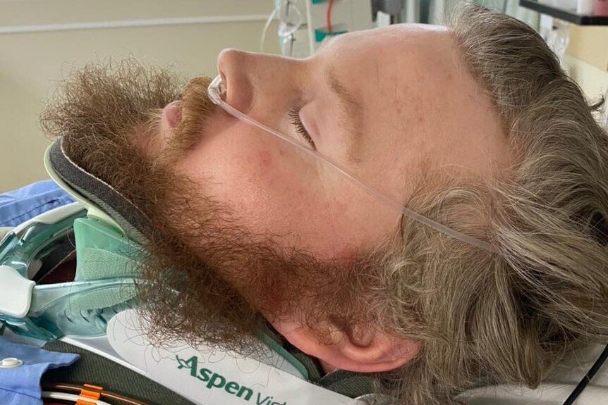 A man lying unconscious in a hospital bed in a neck brace and with breathing tubes after a motorcycle accident.