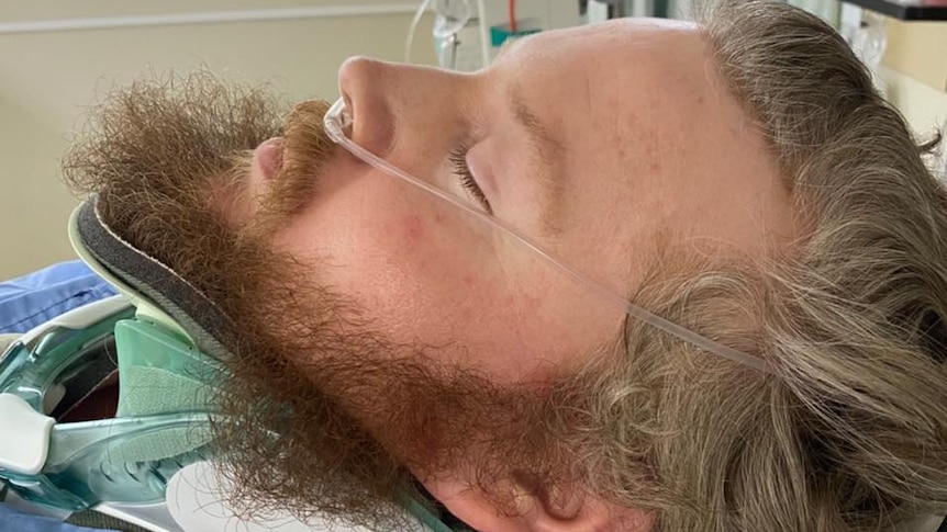 A man lying unconscious in a hospital bed in a neck brace and with breathing tubes after a motorcycle accident.
