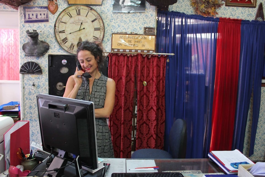 A dark-haired woman smiles while talking on the phone in a room with drapery