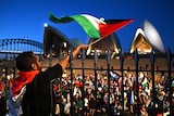 Man in black top waves Palestinian flag in front of Sydney Opera House