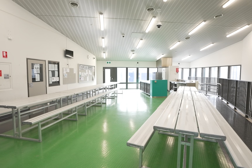 A spacious room with several long tables and benches with a green floor.