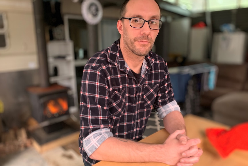 Man sitting at a table, wearing a plaid shirt and glasses.