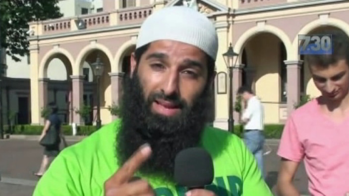 A man holding a microphone points with his finger while talking.