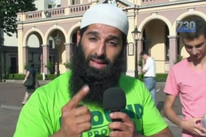 A man holding a microphone points with his finger while talking.