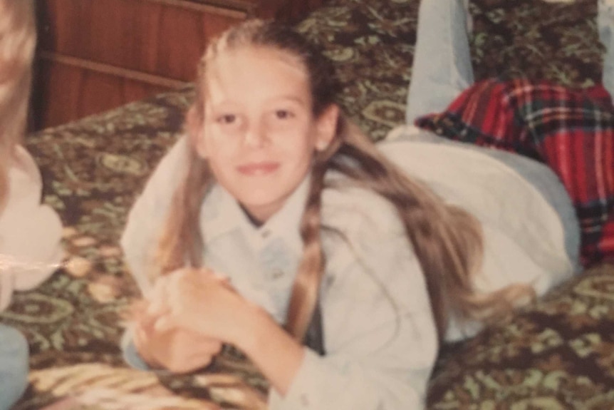 A young girl smiles while lying on a bed reading a book.