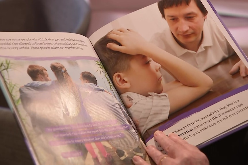 A person holds open a childrens book that shows a photo of a child with his head in his hands. 