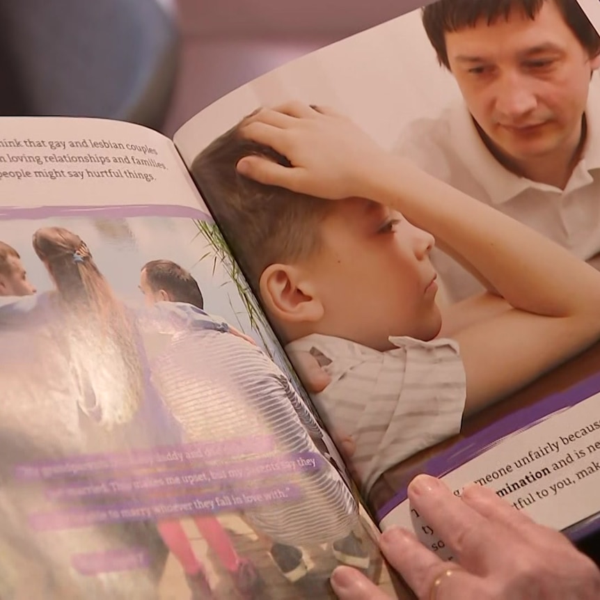 A person holds open a childrens book that shows a photo of a child with his head in his hands. 