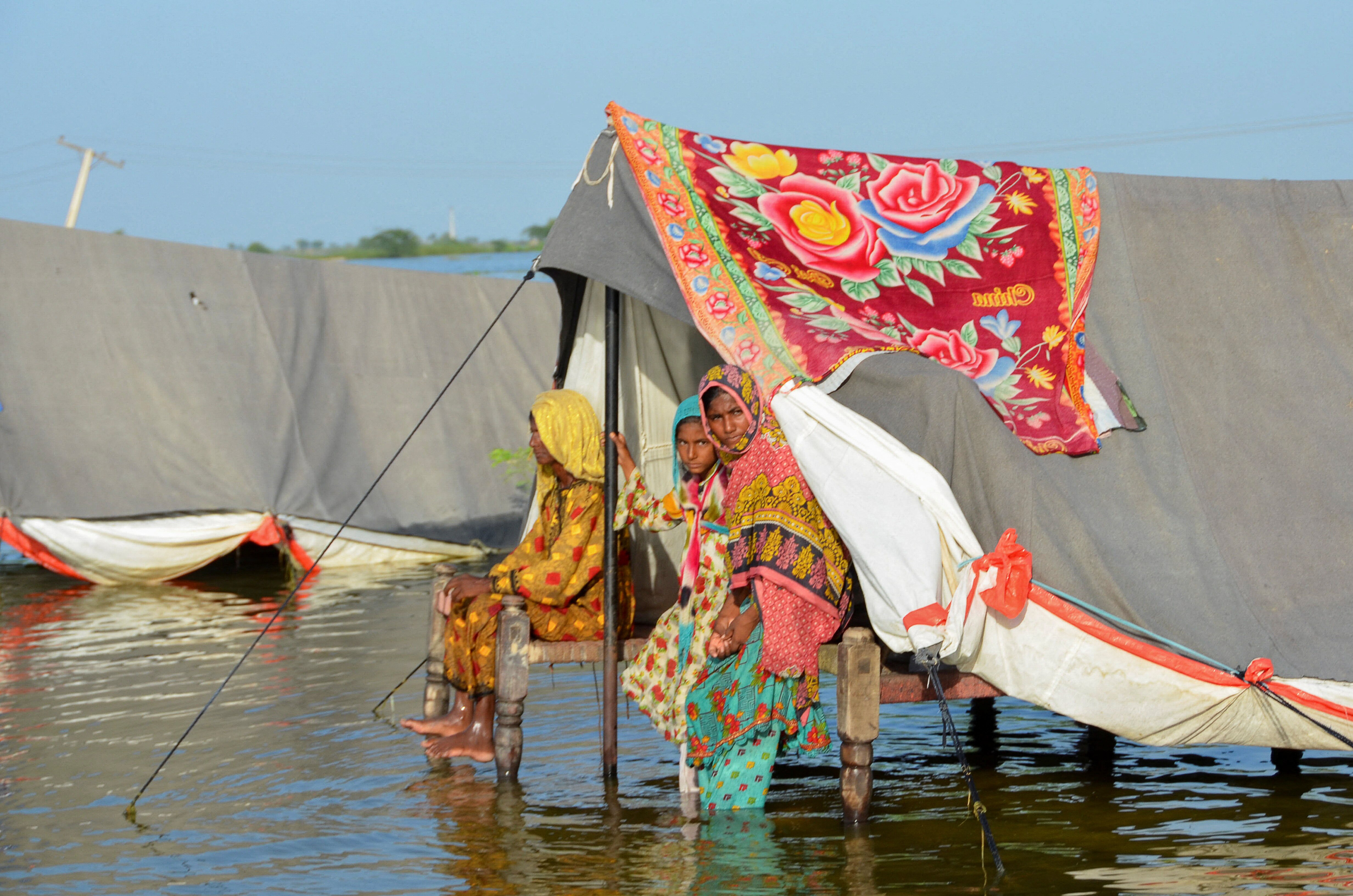 women sit in a tent on stilt, there is water under it. 
