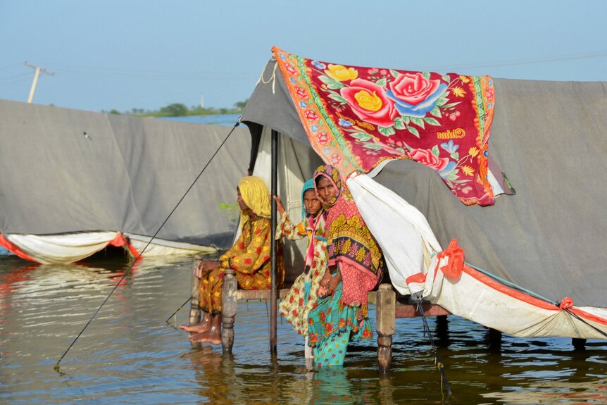 women sit in a tent on stilt, there is water under it. 