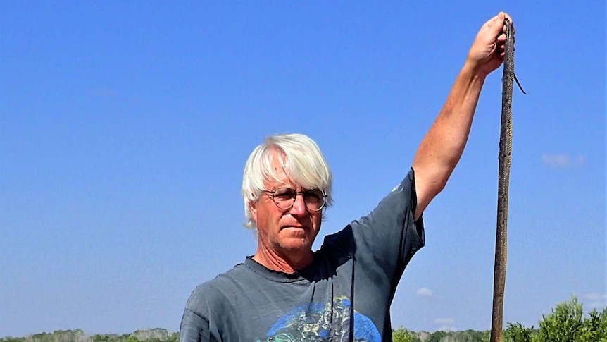 Professor Thomas Madsen on a dam wall holding up a long, thin, and dead water python