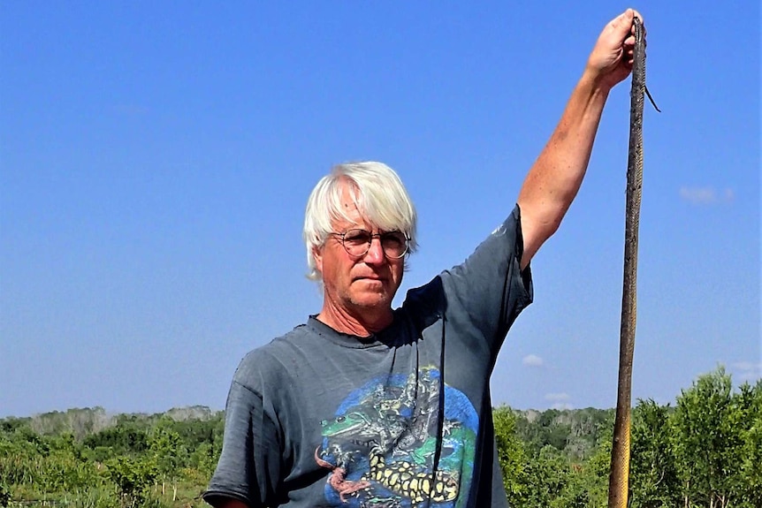 Professor Thomas Madsen on a dam wall holding up a long, thin, and dead water python