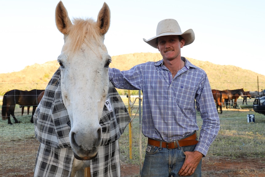 A man wearing a cowboy hat stands next to a white horse.