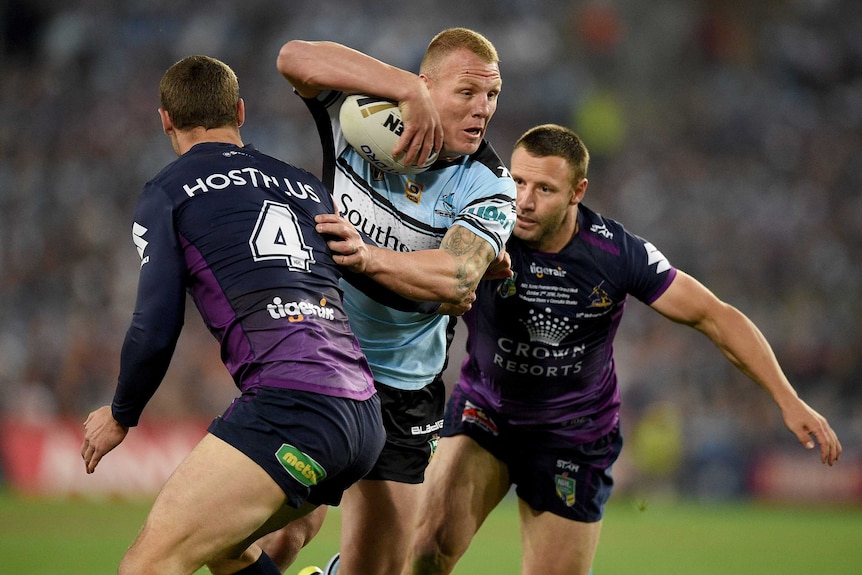 Luke Lewis of the Sharks is tackled by Cheyse Blair and Blake Green of the Storm