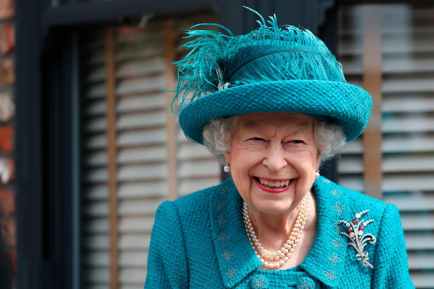 身着蓝色裙子和帽子的伊丽莎白二世女王对着镜头微笑