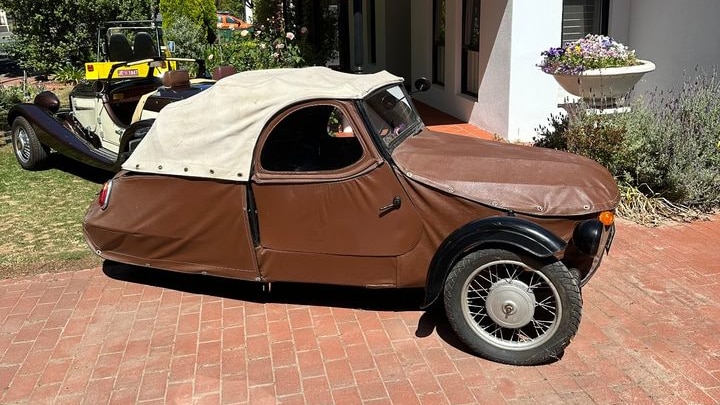 small three-wheeled car with white roof and brown vinyl body in a home driveway