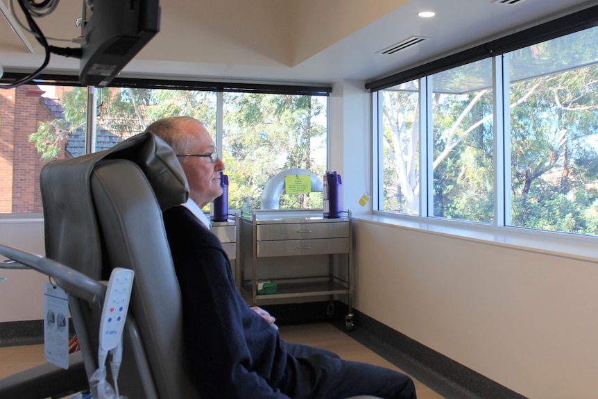 a man sitting down in a chemotherapy lounge, looking out through a window.