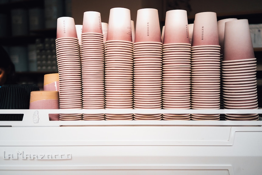 Rows of disposable coffee cups stacked on top of each other, resting on a professional white coffee machine