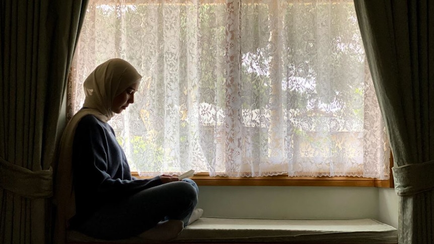 A woman sits alone at home near window and reads a love letter from her husband.