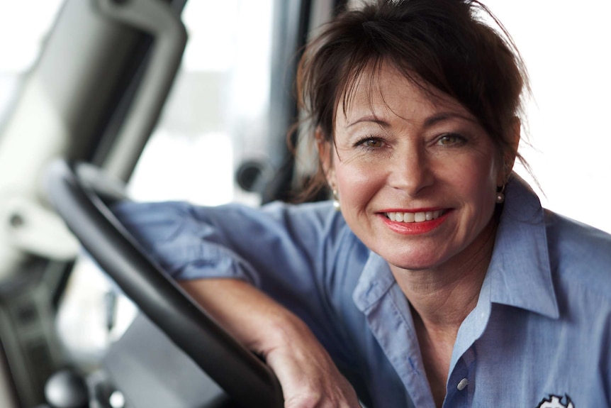 A woman wearing a blue collared shirt leans on the steering wheel of a truck.