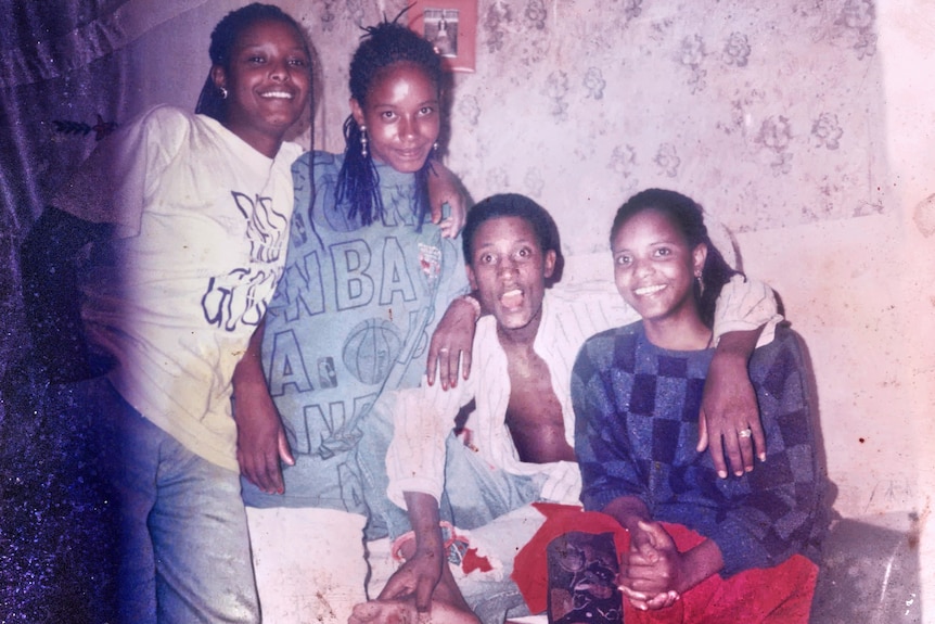 A family of four sit on a couch smiling in an old photo taken on film