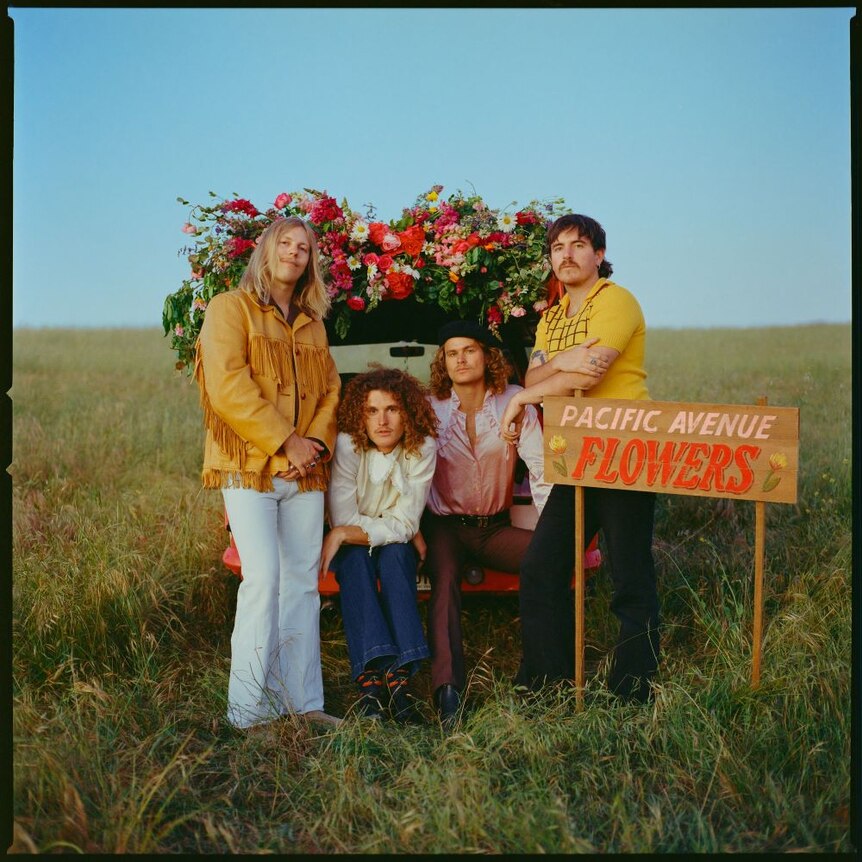 Photograph of the whole band outside with flowers.