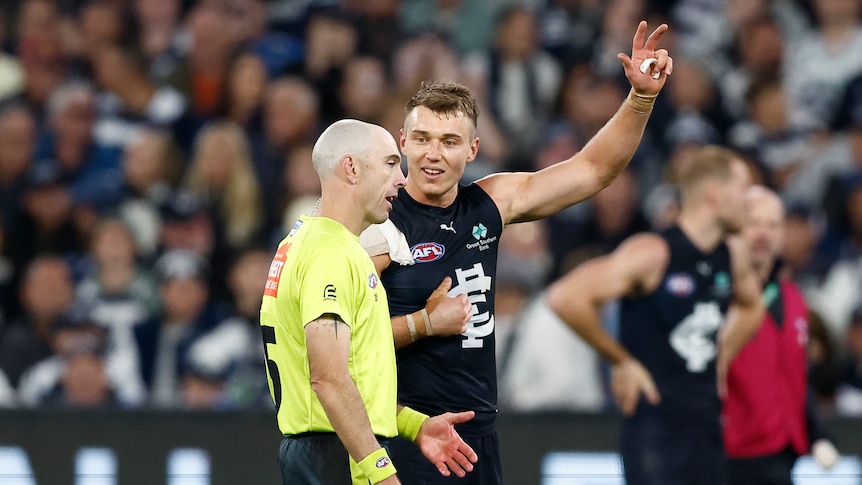 AFL player Patrick Cripps speaking to umpire Mathew Nicholls. Cripps is pointing at himself and holding up an arm