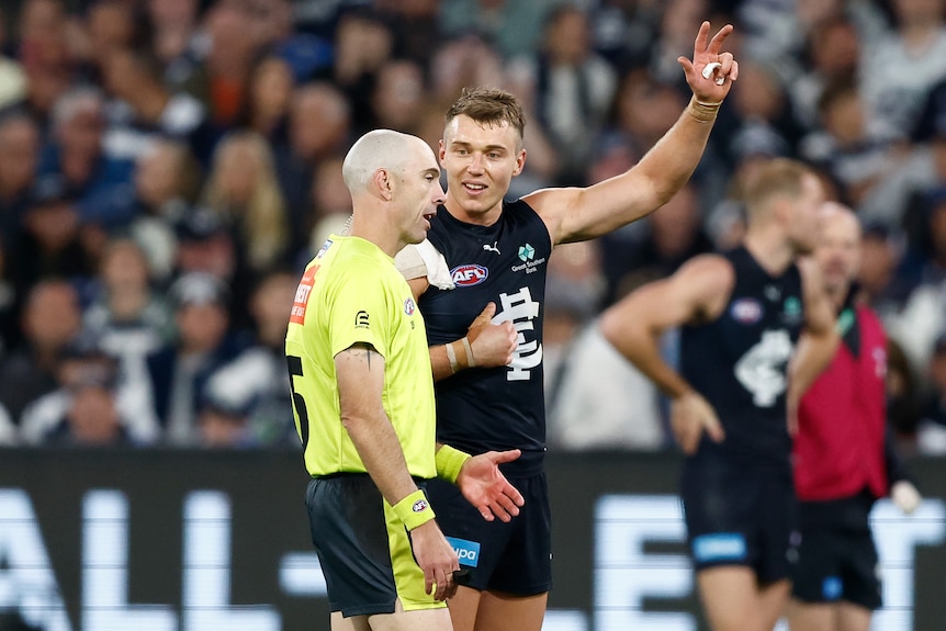 AFL player Patrick Cripps speaking to umpire Mathew Nicholls. Cripps is pointing at himself and holding up an arm