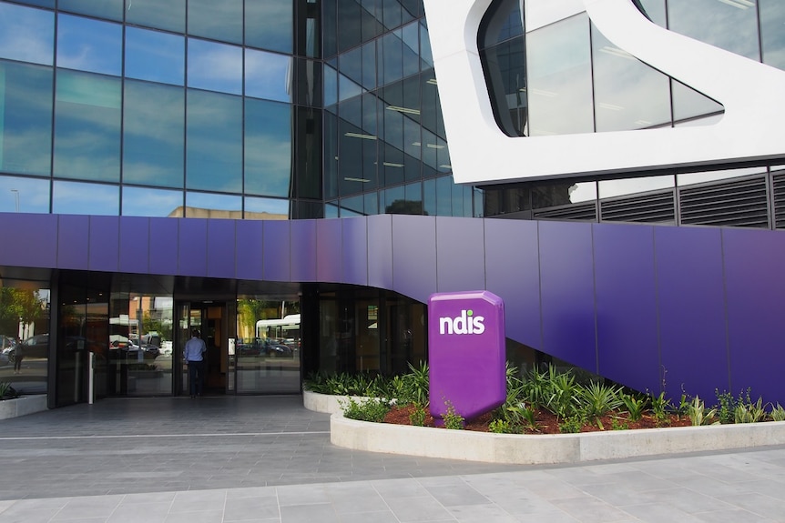 A glass office building with the purple NDIS sign out the front.