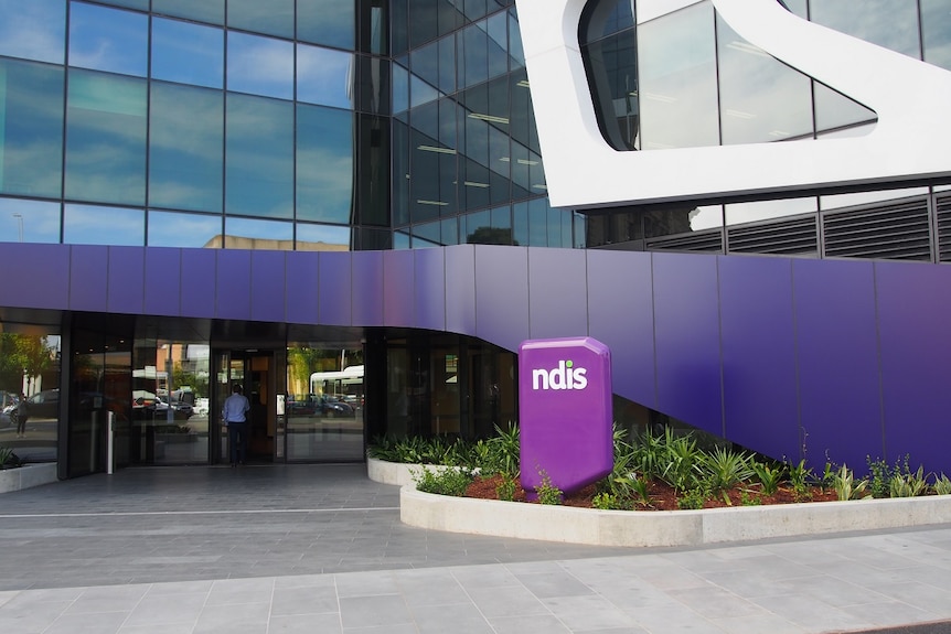 Un edificio de oficinas de vidrio con el letrero violeta del NDIS en el frente.