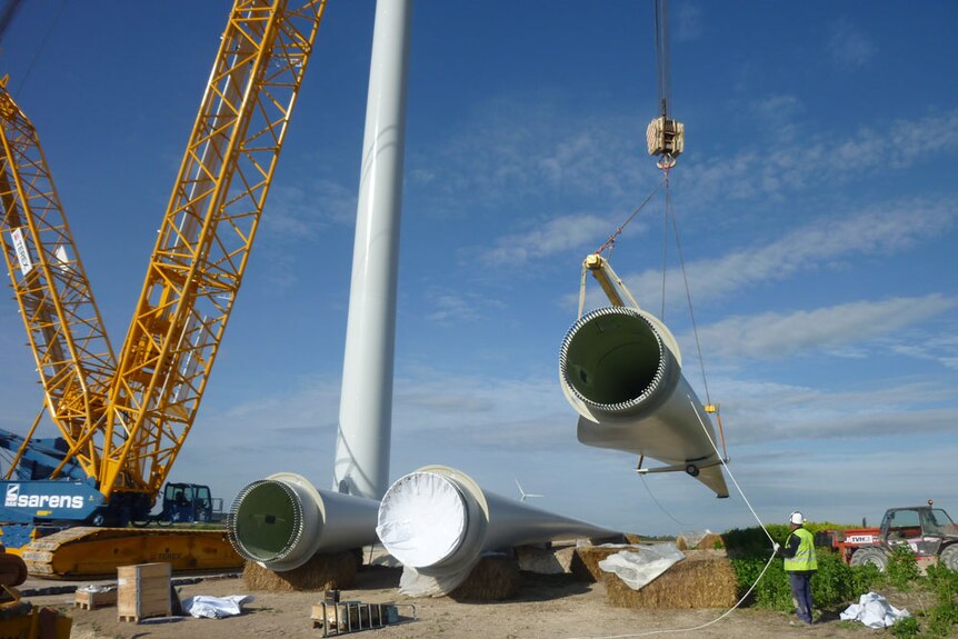 A crane lifts a part of a wind turbine that is being constructed