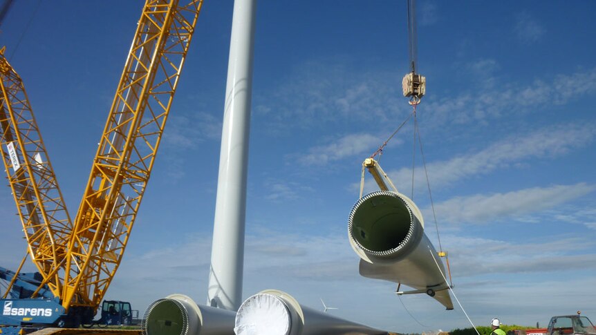 A crane lifts a part of a wind turbine that is being constructed